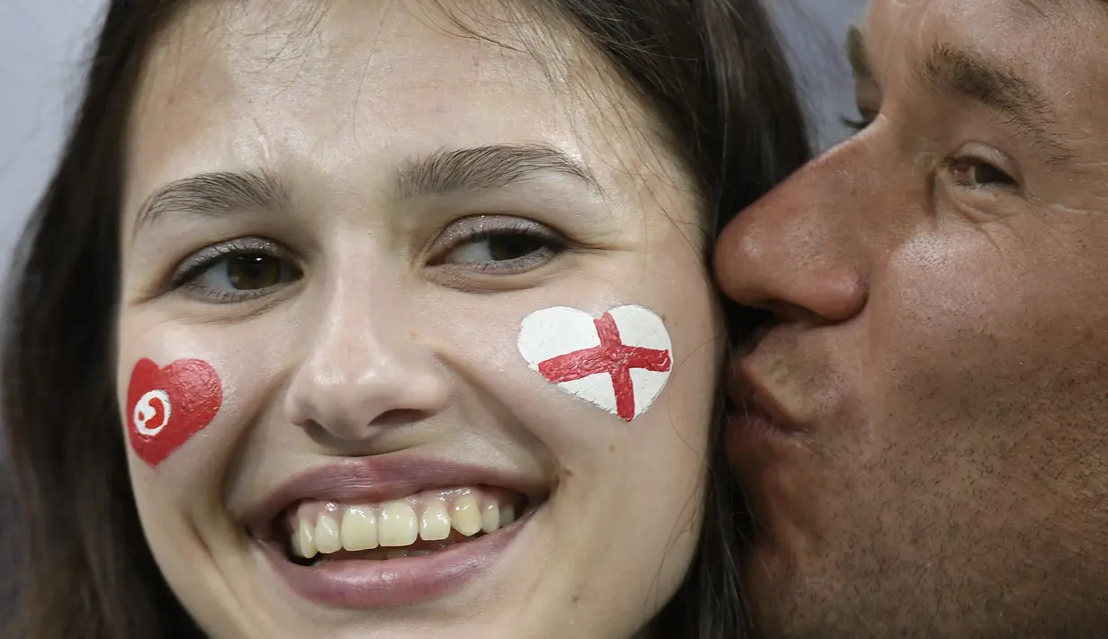 Seorang suporter Inggris mencium kekasihnya saat negaranya melawan Tunisia pada laga grup G Piala Dunia di Volgograd Arena, Volgograd, Senin (18/6/2018). Cerita sepenggal kisah romantis saat Piala Dunia 2018 Rusia. (AFP/Philippe Desmazes)