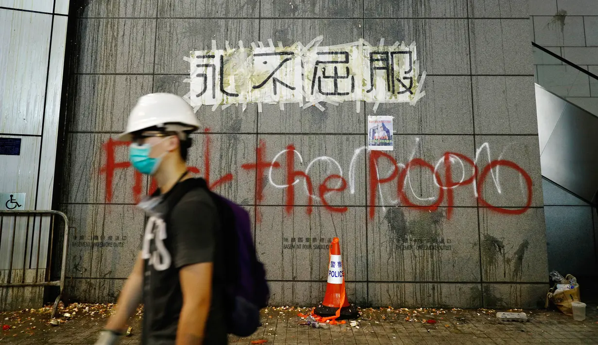 Seorang demonstran berjalan melewati markas polisi yang ditulisi 'Never Give In', Hong Kong, Jumat (21/6/2019). Markas polisi tersebut jadi korban aksi vandalime demonstran dalam lanjutan aksi unjuk rasa menolak RUU Ekstradisi. (AP Photo/Vincent Yu)