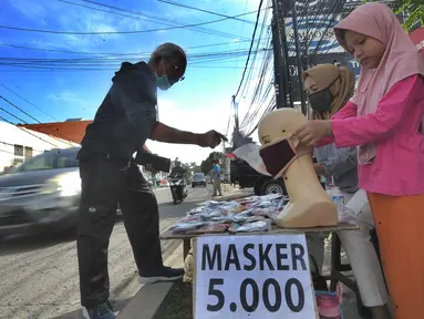 Seorang ibu ditemani anaknya melayani pembeli saat berjualan masker kain buatan rumahan di Jalan Raya Cinere-Depok, Limo, Depok, Rabu (8/4/2020).  Anjuran pemerintah mengenai penggunaan masker kain dimanfaatkan ibu ini untuk berjualan masker kain. (merdeka.com/Arie Basuki)