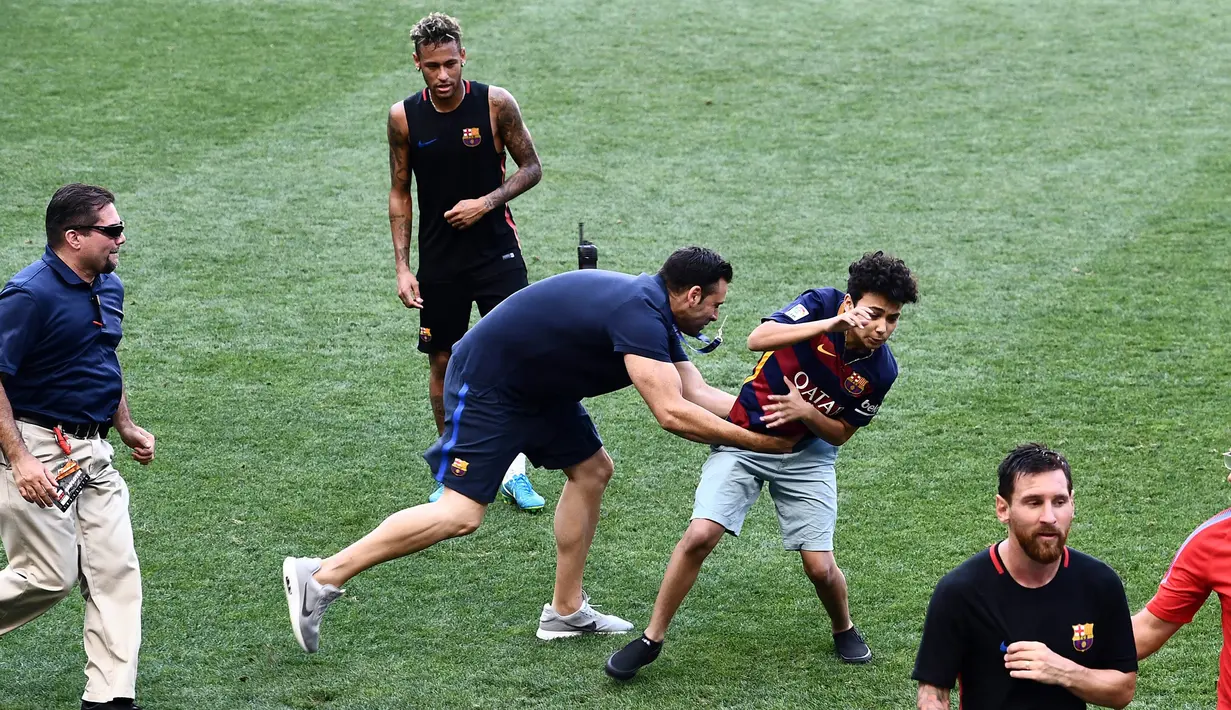 Petugas menangkap fans yang masuk ke lapangan mengejar pemain Barcelona, Lionel Messi dan Neymar saat latihan di Red Bull Arena, New Jersey, Jumat (21/7/2017). Latihan ini dilakukan jelang laga ICC 2017 melawan Juventus. (AFP/Jewel Samad)