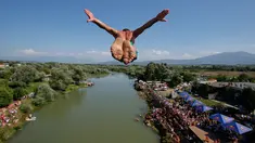 Penonton menyaksikan dari tepi sungai saat seorang peserta melakukan terjun bebas dari jembatan Ura e Shejnt dalam kompetisi menyelam tradisional ke-68 di Gjakova, Kosovo, 22 Juli 2018. Kompetisi ini dilakukan dari ketinggian 22 meter. (AP/Visar Kryeziu)