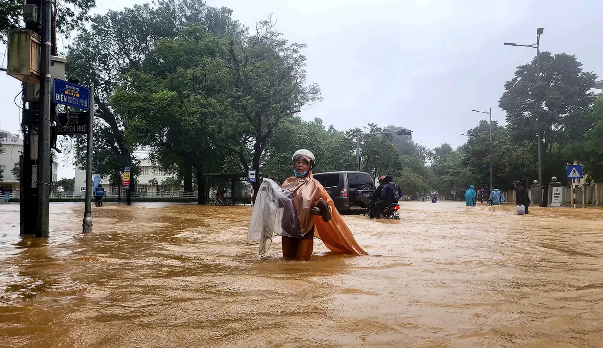 Seorang perempuan berjas hujan mengarungi jalanan yang tergenang banjir di Hue pada 28 Oktober 2025. Ribuan warga dievakuasi setelah curah hujan lebih dari 1.000 milimeter (mm) dalam 24 jam terakhir yang membanjiri kota di wilayah tengah Vietnam itu. (Foto oleh AFP)