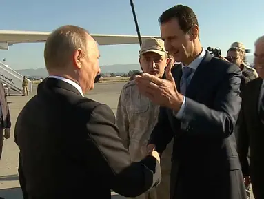 Presiden Suriah Bashar Assad bersalaman dengan Presiden Rusia, Vladimir Putin saat tiba di pangkalan udara Hemeimeem di Suriah (11/12). Putin menyatakan akan menarik pasukan Rusia di Suriah. (Presidential TV photo via AP)