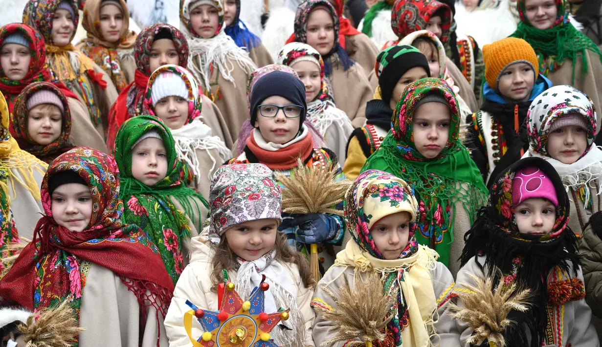 Mengenakan pakaian tradisional, warga Ukraina bernyanyi bersama sambil membawa 'Didukh'. 'Didukh' merupakan simbol Natal tradisional Ukraina. Tampak dalam foto, anak-anak yang mengenakan pakaian tradisional dan membawa hiasan tradisional Natal Ukraina 'Didukh' dalam prosesi Malam Natal di Lviv pada 24 Desember 2025. (YURIY DYACHYSHYN/AFP)