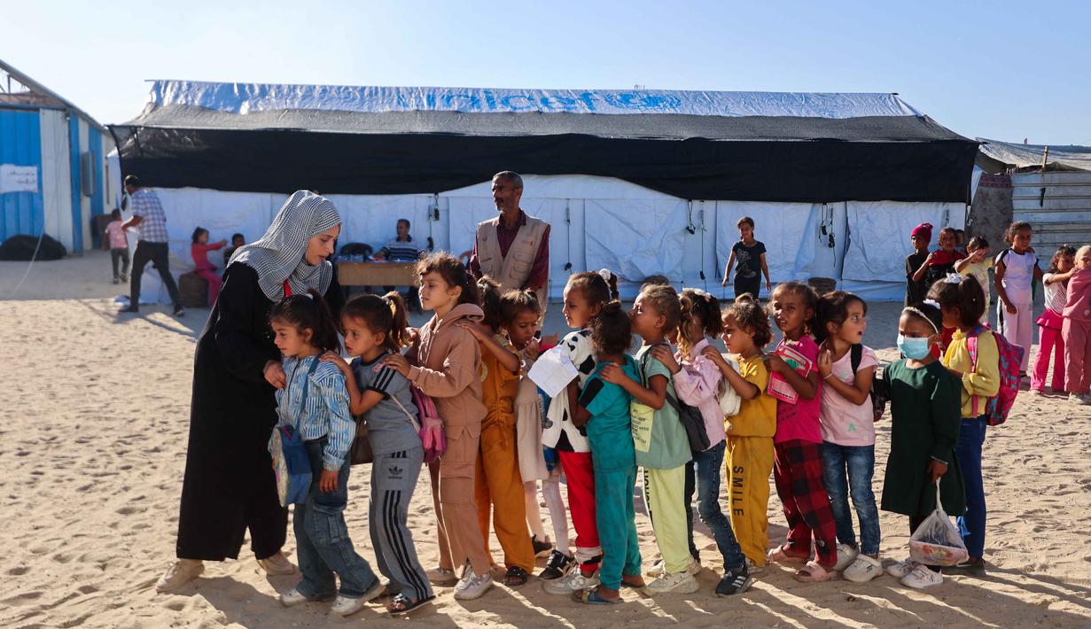 Guru-guru Palestina membariskan murid-murid di halaman sekolah yang didirikan oleh Asosiasi Kebudayaan Mayasem dengan dukungan UNICEF, sebelum pelajaran di kamp pengungsian di kawasan al-Qarara, Khan Yunis, di bagian selatan Jalur Gaza pada Selasa 7 Oktober 2025. (Omar AL-QATTAA/AFP)