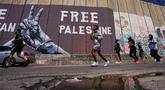Para pelari melewati tembok pemisah Israel saat mereka berkompetisi dalam Maraton Palestina di kota Betlehem, Tepi Barat, Jumat 8 Mei 2026. Maraton Internasional Palestina kembali dilaksanakan pada Jumat 8 Mei 2026, di kota Betlehem, Tepi Barat. (AP Photo/Mahmoud Illean)