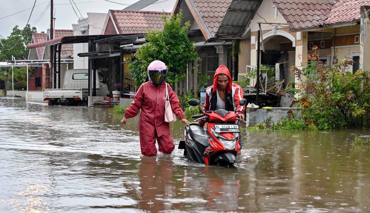 Sejak akhir pekan lalu, Banjir terjadi di sembilan wilayah di Aceh. Tampak dalam foto, seorang pria mendorong sepeda motornya menerobos banjir di jalan yang tergenang setelah hujan deras di permukiman Darul Imarah, pinggiran Banda Aceh, pada Kamis 27 November 2025. (CHAIDEER MAHYUDDIN/AFP)