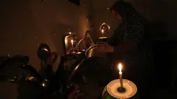 Seorang wanita Palestina mencuci piring dengan menggunakan penerangan lilin selama pemadaman listrik di kamp pengungsian Rafah, Jalur Gaza selatan, 11 Juni 2017. Selama ini Gaza menerima pasokan listrik Israel selama 3,5 jam setiap hari. (SAID KHATIB/AFP)