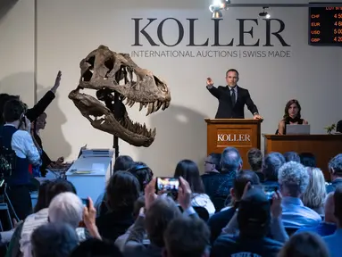 Direktur rumah lelang Koller Cyril Koller (Tengah) memberi isyarat di sebelah tengkorak 'Trinitas' selama penjualan kerangka Tyrannosaurus-Rex (T-Rex) oleh rumah lelang Koller di Zurich, pada 18 April 2023. (Photo by Fabrice COFFRINI / AFP)