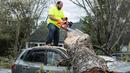 Seorang pria menebang batang pohon yang menimpa mobilnya usai terjadi badai di Elon, Virginia (16/4). Akibat badai ini sejumlah rumah rusak berat. (Jay Westcott/The News & Advance via AP)