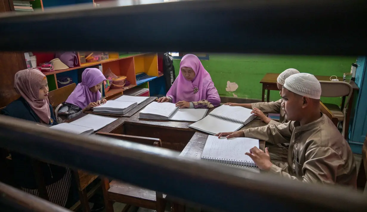 Para siswa tersebut menggerakkan ujung jari mereka di atas serangkaian titik timbul yang mewakili huruf-huruf hijaiyah. Tampak dalam foto, para siswa tunanetra membaca Al-Quran dalam huruf Braille selama bulan suci Ramadan 1447 Hijriah di sebuah sekolah di Surabaya, Jawa Timur, pada 27 Februari 2026. (JUNI KRISWANTO/AFP)