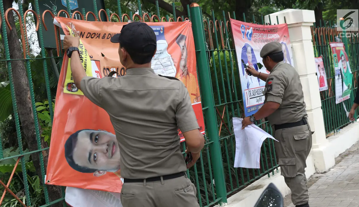 <p>Petugas Satpol PP bersama Panwaslu kecamatan Ciracas menurunkan APK yang terpasang di pagar pembatas antara jalan dengan taman di pinggir kali di sekitar Jalan Raya Bogor, Jakarta, Rabu (23/1). (Liputan6.com/Helmi Fithriansyah)</p>