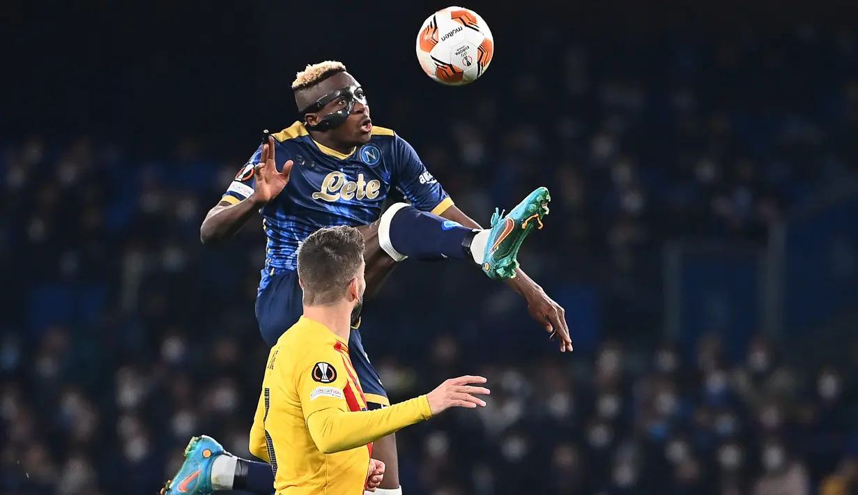 Pemain depan Napoli Victor Osimhen melompat di sebelah bek Barcelona Gerard Piquegur pada play-off fase gugur Liga Europa 2021/2022 di Stadion Diego Armando Maradona, Jumat (25/2/2022) dini hari WIB. Barcelona melaju ke babak 16 besar usai menang telak 4-2 di kandang Napoli. (ANDREAS SOLARO/AFP)