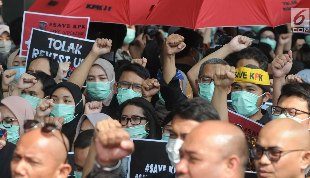 Pegawai KPK membawa poster saat menggelar aksi di Lobi Gedung KPK, Kuningan, Jakarta, Jumat (6/9/2019). Dalam aksi menolak revisi UU KPK tersebut, mereka mengenakan baju serba hitam lengkap dengan masker penutup mulut dan memasang KPK Lines di sekitar pintu masuk. (merdeka.com/Dwi Narwoko)