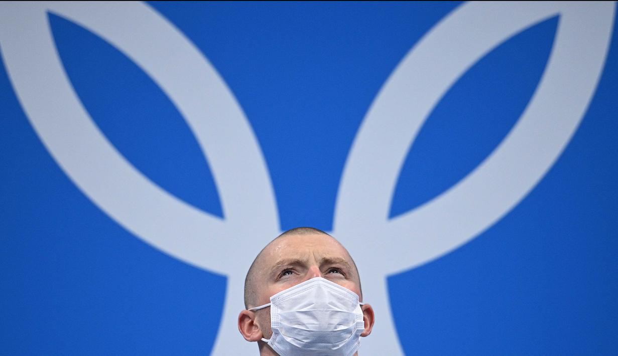 Atlet renang asal Inggris, Adam Peaty berdiri di podium saat akan menerima medali emas usai pertandingan final gaya dada 100m renang putra Olimpiade Tokyo 2020 di Tokyo Aquatics Center, Senin (26/7/2021). (Foto: AFP/Oli Scarff)
