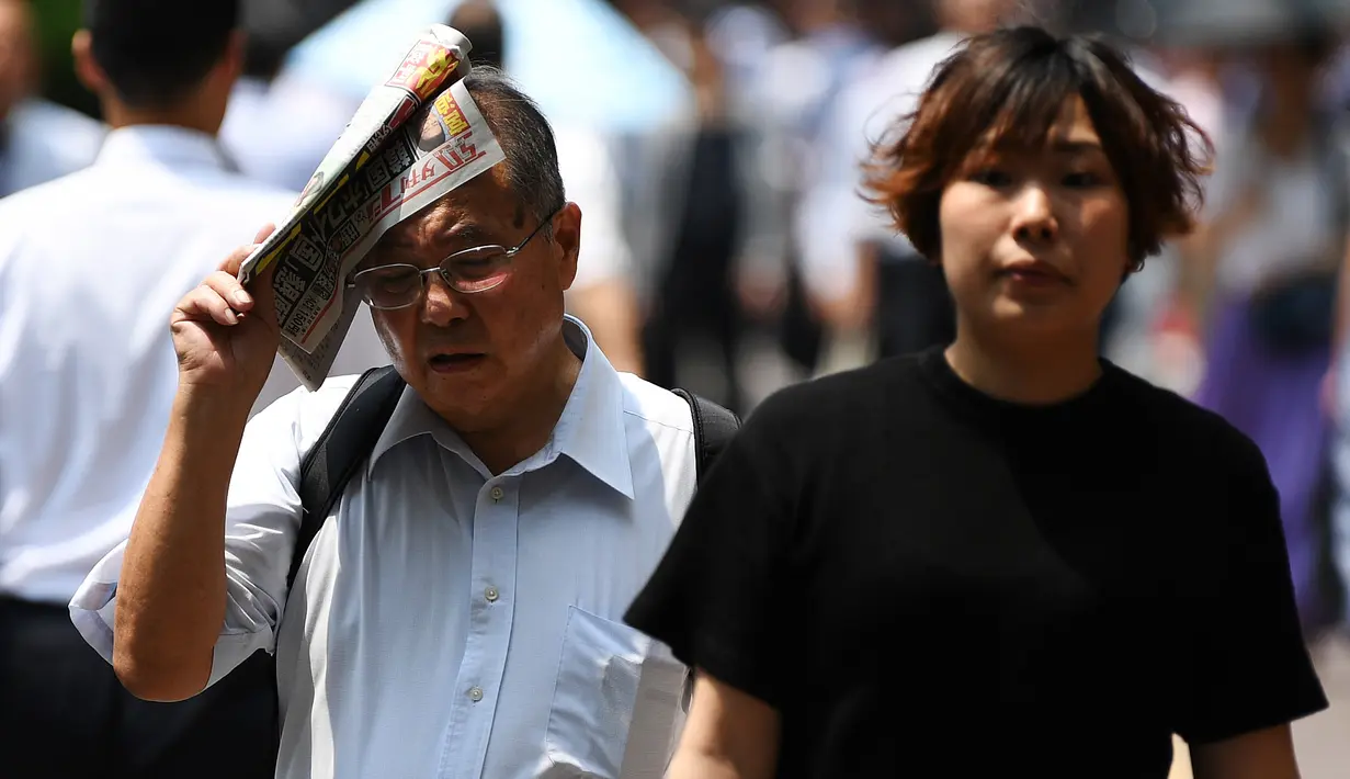 Seorang pria melindungi dirinya dari sinar matahari dengan sebuah koran saat gelombang panas di Tokyo, Jepang (1/7/2019). Cuaca panas ekstrem yang melanda Jepang telah menewaskan puluhan orang tewas dan menyebabkan ribuan orang masuk rumah sakit dengan gejala dehidrasi. (AFP Photo/Charly Triballeau)