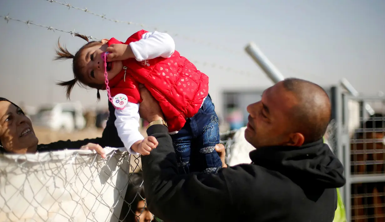 Seorang pria menyeberangkan anak perempuan melewati kawat berduri di kamp pengungsian Khazer, Irak (28/11). Mereka pergi meninggalkan daerah yang sebelumnya dikuasai kelompok militan ISIS untuk mengungsi ke tempat yang lebih aman. (Reuters/Mohammed Salem)