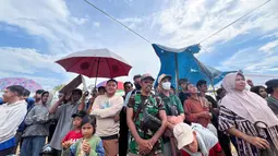 Warga yang hadir rela berpanas-panasan ketika suhu udara mencapai 36 derajat celsius. Demi melindungi kepala dari terik matahari, mereka menggunakan payung hingga spanduk. (Bola.com/M Iqbal Ichsan)