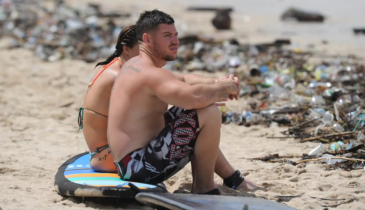 Turis duduk di atas papan selancar di pesisir Pantai Kuta yang dikelilingi oleh puing-puing dan sampah, Bali, Minggu (9/12). Kawasan pantai Kuta kembali dipenuhi oleh sampah hanyut terbawa oleh gelombang. (SONNY TUMBELAKA / AFP)