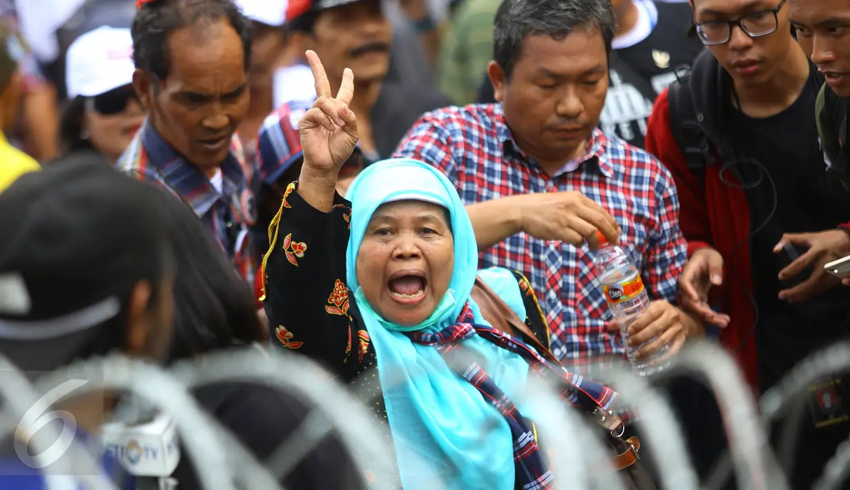Pendukung Cagub DKI Basuki T Purnama memberikan salam dua jari saat sidang kasus penistaan agama, Jakarta, Selasa (10/1). Dengan mengenakan atribut kotak-kotak, massa membawa bendera Indonesia serta melakukan orasi damai. (Liputan6.com/Immanuel Antonius)