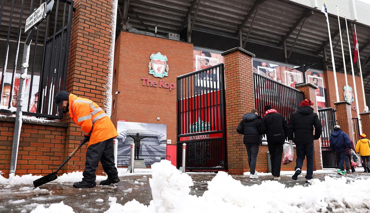 Seorang petugas membersihkan salju di sekitar area Stadion Anfield menjelang laga lanjutan Liga Inggris 2024/2025 antara Liverpool melawan Manchester United pada Minggu (05/01/2025). (AFP/Darren Staples)