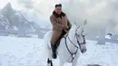 Pemimpin Korea Utara Kim Jong-un tersenyum saat berada di atas kuda putih saat salju turun di gunung Paektu (16/10/2019). Kim Jong-un tampil mengenakan kaca mata dengan mantel tebal berwarna coklat.  (Photo by STR/KCNA VIA KNS/AFP)