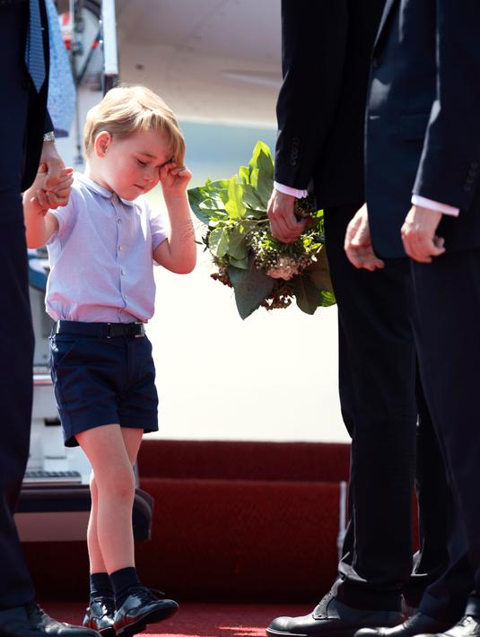 Pangeran George mengusap matanya sambil menggenggam tangan sang ayah, Pangeran William setibanya di Bandara Tegel, Berlin, Rabu (19/7). George ikut dalam tur keluarga kerajaan Inggris bersama Pangeran William dan Kate Middleton. (Kay Nietfeld/dpa via AP)