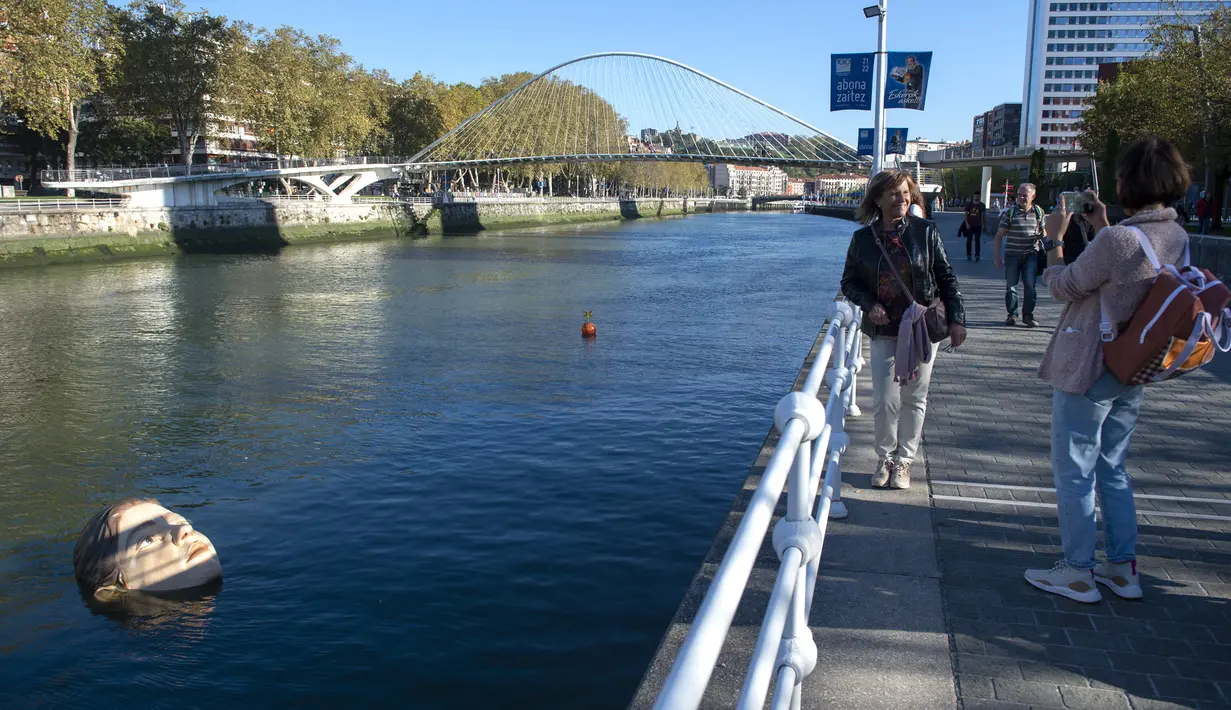 Dua wanita mengambil gambar patung Bihar karya seniman hiperrealis asal Meksiko Ruben Orozco terendam di Sungai Nervion, Kota Bilbao, Basque, Spanyol, 14 Oktober 2021. Bihar diambil dari kata dalam bahasa Basque yang artinya 'besok'. (ANDER GILLENEA/AFP)