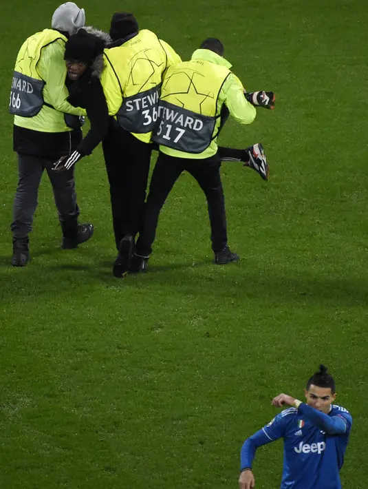Penyerang Cristiano Ronaldo berjalan meninggalkan seorang penggemar yang masuk menghampirinya selama pertandingan antara Lyon dan Juventus pada leg pertama babak 16 Liga Champions di Stadion Olimpiade Lyon di Decines, Prancis (26/2/2020). (AFP/Jean-Philippe Ksiazek)