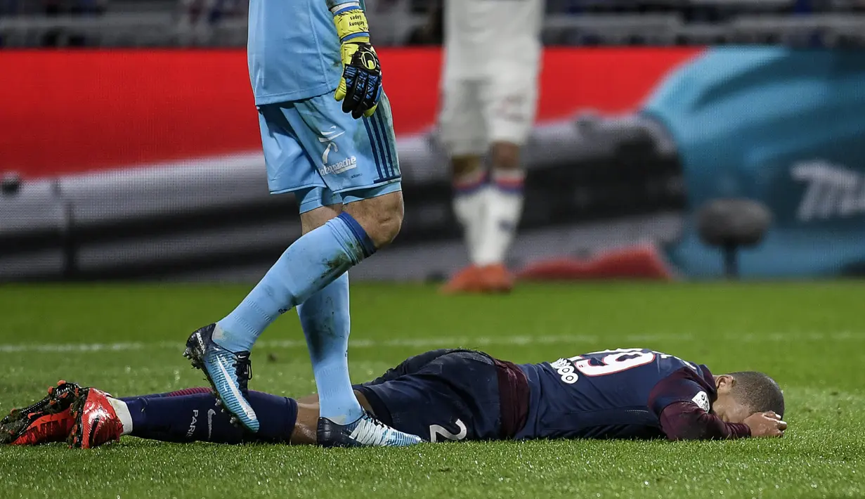 Pemain Paris Saint-Germain, Kylian Mbappe tersungkur di lapangan saat lanjutan Ligue 1 di Groupama Stadium, Senin (22/1). Mbappe mengalami cedera setelah berbenturan dengan kiper Olympique Lyon, Anthony Lopes. (AFP PHOTO / JEFF PACHOUD)