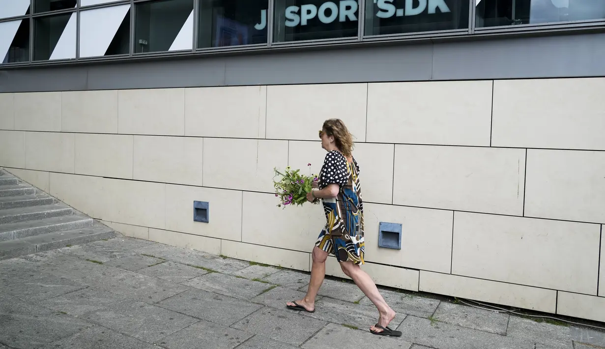 Seorang wanita membawa seikat bunga untuk meninggalkannya pada pintu masuk pusat perbelanjaan Field di Kopenhagen, Denmark, 4 Juli 2022. Polisi mengesampingkan bahwa serangan hari Minggu itu terkait dengan terorisme. (AP Photo/Sergei Grits)