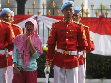 Seorang warga berfoto diantara anggota Paspampres di depan Istana Negara, Jakarta, Minggu (17/7). Prosesi pergantian pasukan penjaga Istana Negara merupakan kegiatan rutin yang dilangsungkan pada Minggu ke-2 tiap bulannya. (Liputan6.com/Gempur M Surya)