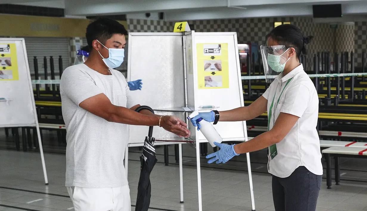 Petugas membersihkan tangan pemilih usai dia memberikan suaranya dalam pemilu di TPS Sekolah Tinggi Chung Cheng, Singapura, Jumat (10/7/2020). Pemilu di tengah pandemi COVID-19, warga Singapura memberikan suara mereka dengan mengenakan masker dan sarung tangan plastik. (AP Photo)