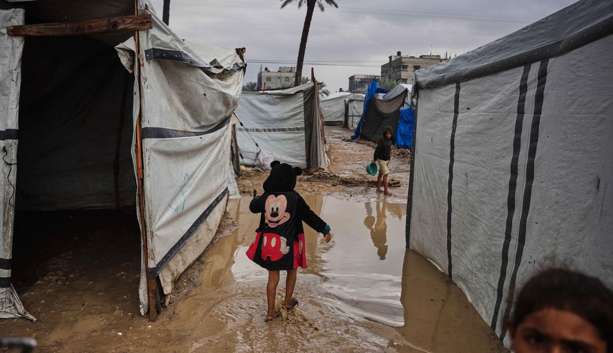 Situasi ini memperburuk kehidupan warga Gaza yang tinggal di lokasi penampungan. Tampak dalam foto, warga Palestina berjalan melewati tenda-tenda sementara yang terendam banjir setelah hujan deras di Deir al-Balah, Jalur Gaza tengah, Selasa 25 November 2025. (AP Photo/Abdel Kareem Hana)