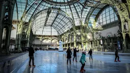 Orang-orang  berseluncur di arena ice skating di bawah kubah kaca mewah legendaris, Grand Palais, Paris, Senin (17/12). Tempat seluas 1.800 meter persegi ini menjadi arena ice skating sementara terbesar di Prancis. (STEPHANE DE SAKUTIN / AFP)
