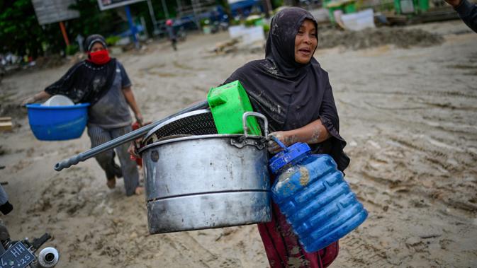 Penduduk desa membawa barang-barang dari rumah mereka sebelum mengungsi setelah banjir bandang di Kabupaten Luwu Utara, Sulawesi Selatan, Rabu (15/7/2020).  Akibat banjir bandang tersebut mengakibatkan 16 orang meninggal dunia dan ratusan rumah tertimbun lumpur. (Hariandi HAFID / AFP)