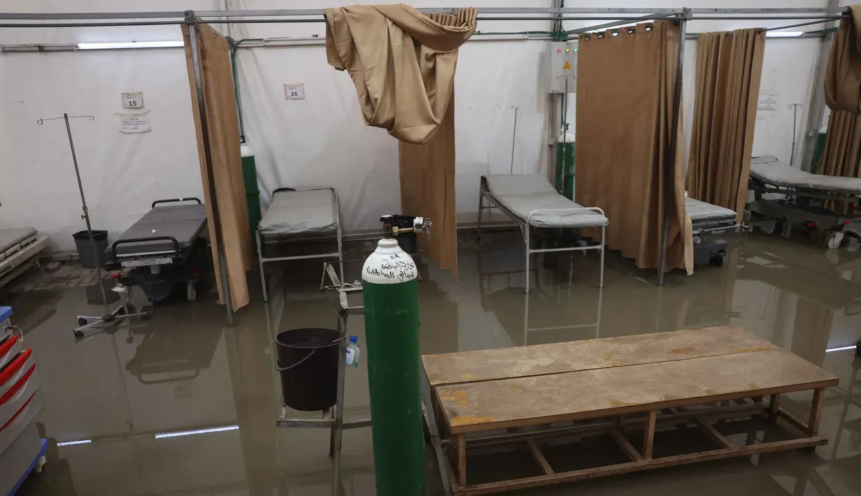 Kondisi ini memperparah krisis kemanusiaan di wilayah tersebut. Tampak dalam foto, ranjang-ranjang kosong di dalam tenda darurat milik Rumah Sakit Nasser, yang berfungsi sebagai tempat penerimaan pasien rawat jalan dan departemen gawat darurat, setelah hujan lebat di Khan Yunis di Jalur Gaza selatan pada 26 Maret 2026. (Bashar Taleb/AFP)