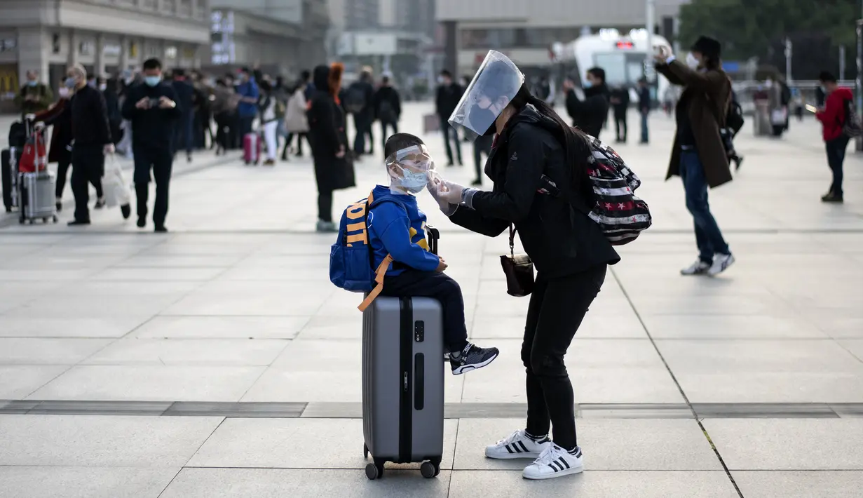 Seorang wanita yang mengenakan masker, sarung tangan, dan pelindung wajah menyesuaikan masker anaknya di Stasiun Hankou, Wuhan, Hubei, China, Rabu (8/4/2020). Setelah pandemi virus corona COVID-19 mereda, banyak warga di Wuhan beraktivitas memakai alat pelindung diri. (NOEL CELIS/AFP)