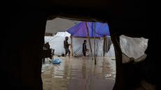 Para pengungsi Palestina berjalan melewati kamp tenda yang basah kuyup akibat hujan lebat di Deir al-Balah, Jalur Gaza tengah, Kamis, 26 Maret 2026. Kondisi kamp pengungsian di Gaza sangat memprihatinkan akibat banjir yang terus berulang selama musim dingin. (AP Photo/Abdel Kareem Hana)