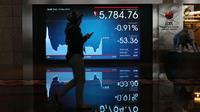 Pekerja melintasi layar pergerakan Indeks Harga Saham Gabungan (IHSG) di BEI, Jakarta, Rabu (16/5). Meski terjebak di zona merah, IHSG berhasil mengakhiri perdagangan di level 5.841. (Liputan6.com/Angga Yuniar)
