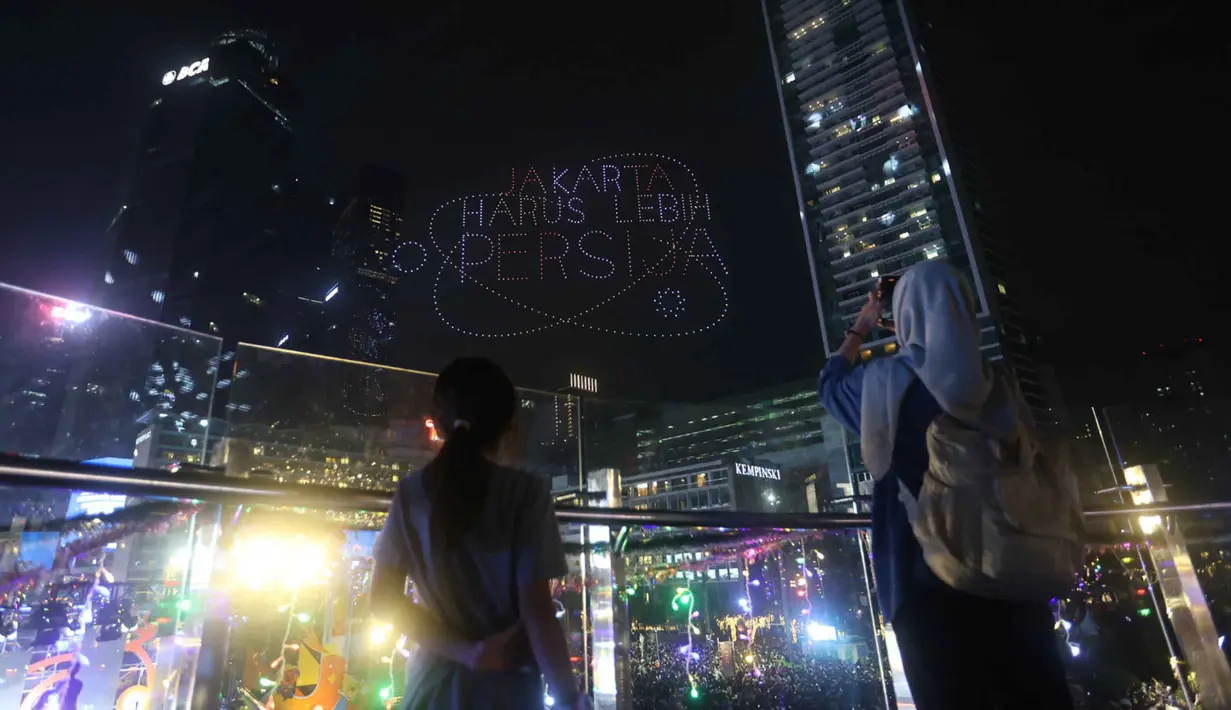 Dan ketika, visual drone membentuk tulisan “Jakarta Harus Lebih Persija”, warga antusias memberikan tepuk tangan dan sorakan meriah. Tampak dalam foto, warga mengabadikan pertunjukan drone saat perayaan malam pergantian tahun di kawasan Bundaran Hotel Indonesia, Jakarta, Rabu (31/12/2025). (Kapanlagi.com/Budy Santoso)