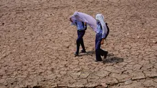 Anak-anak sekolah menggunakan handuk katun di atas kepala mereka untuk melindungi diri dari terik matahari saat berjalan melintasi ladang kering di pinggiran Jammu, India, Rabu 20 Mei 2026. (AP Photo/Channi Anand)
