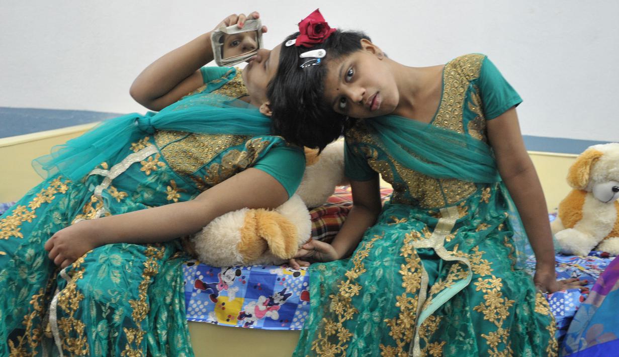 Veena (kanan) menggunakan cermin untuk melihat adiknya Vani saat berada di Rumah Anak di Hyderabad, India (2/1). Veena dan Vani adalah kembar siam dengan kepala yang menempel.  (AFP/Noah Seelam)