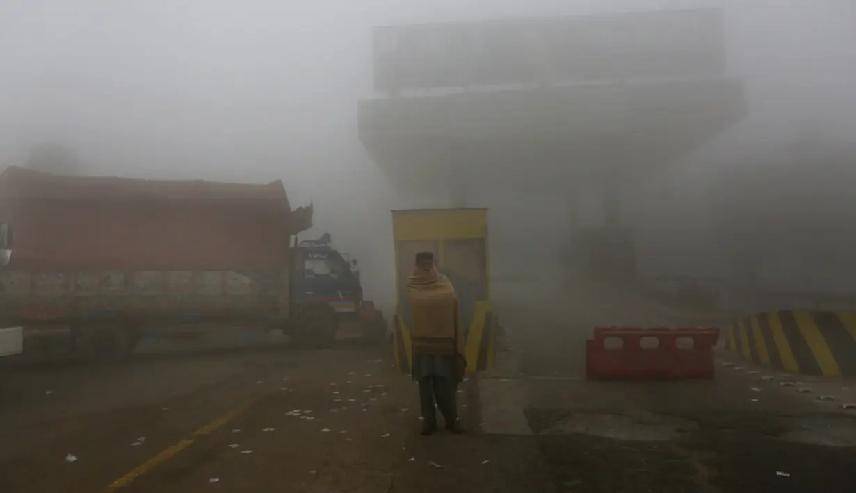 Seorang pengemudi berdiri di samping truknya saat menunggu pembukaan jalan raya yang ditutup karena kabut tebal di Lahore, Pakistan, 15 Desember 2021. Kabut tebal membuat kendaraan harus melaju lambat karena jarak pandang berkurang. (AP Photo/K.M. Chaudary)