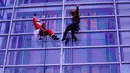 Dua petugas pembersih kaca jendela berkostum Santa Claus dan rusa melambaikan tangan di gedung bertingkat pusat perbelanjaan di Tokyo, Kamis (21/12). Para pekerja ini berbagi kecerian Natal dalam bentuk yang berbeda. (AP/Shizuo Kambayashi)