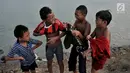 Anak-anak tertawa saat berpakaian usai berenang di Danau Sunter, Jakarta, Selasa (23/7/2019). Anak-anak tetap nekat berenang di Danau Sunter kendati mereka sadar telah dilarang dan dapat membahayakan diri sendiri. (merdeka.com/Iqbal Nugroho)