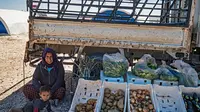 Seorang wanita Suriah yang terlantar duduk bersama putranya di sebelah kios sayur-mayurnya selama bulan suci Ramadan di kamp Washukanni untuk para pengungsi internal di provinsi Hasakeh di timur laut Suriah, (10/5/2020). (AFP/Delil Souleiman)