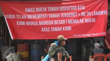 Seorang ibu menggendong anaknya berjalan di depan spanduk penolakan di kawasan jalan Mangga Besar, Jakarta, Senin (22/8). Spanduk itu dipasang warga RW2 Kelurahan Mangga Besar sebagai aksi menolak penggusuran rumah mereka. (Liputan6.com/Gempur M Surya)