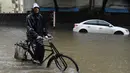 Seorang pria melintasi banjir dengan sepeda setelah hujan lebat di Mumbai, India (9/7). Mumbai dan daerah pinggiran lainnya telah mengalami hujan lebat semalaman yang mengakibatkan banjir. (AFP Photo/Indranil Mukherjee)
