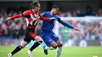Gelandang Brentford, Mathias Jensen mencoba merebut bola dari kaki bek Chelsea, Levi Colwill dalam laga Premier League 2023/2024 di Stamford Bridge, Sabtu (28/10/2023) malam WIB. (AFP/Justin Tallis)